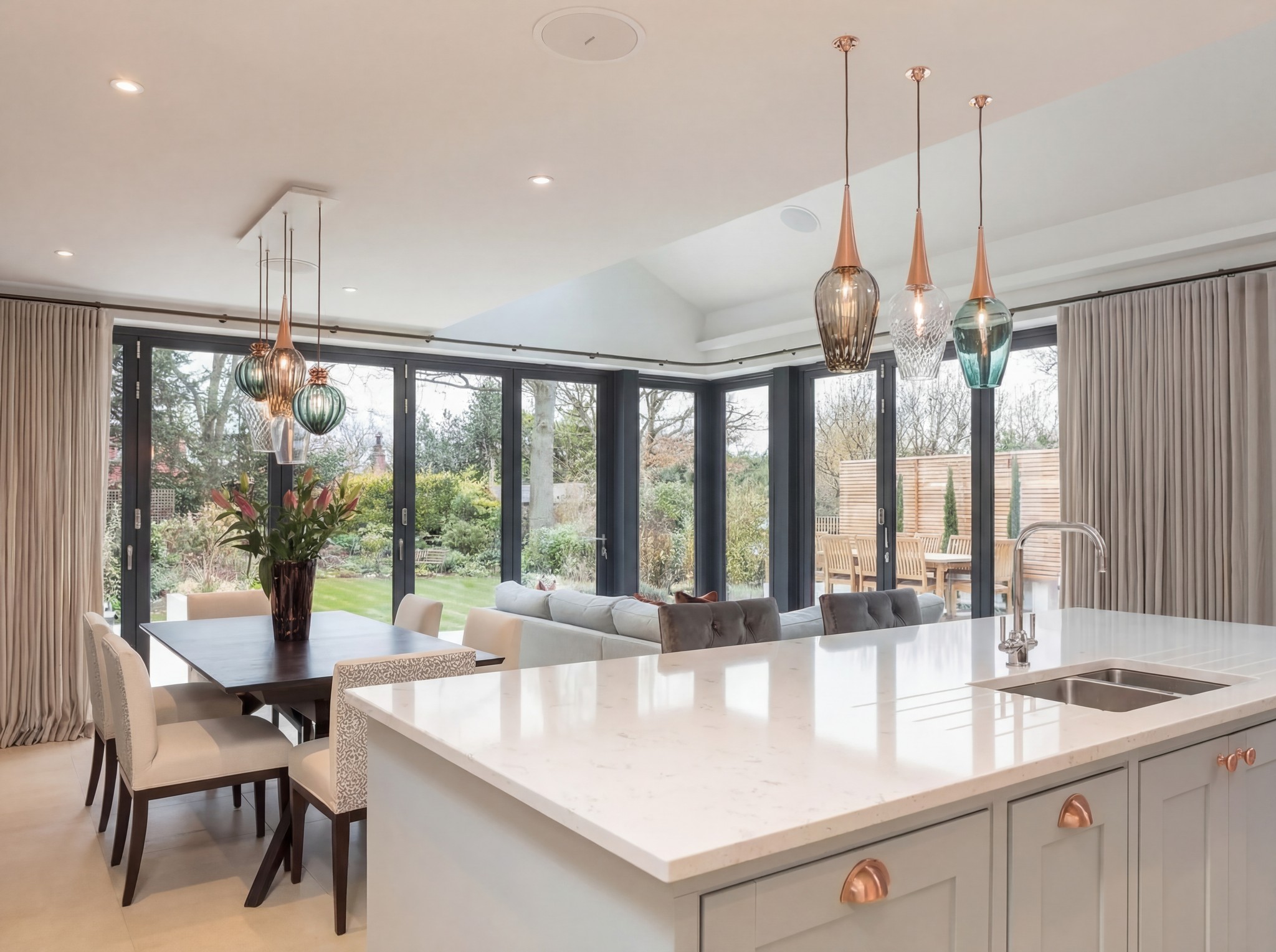 Open-plan kitchen with a white island, copper pendants and garden doors