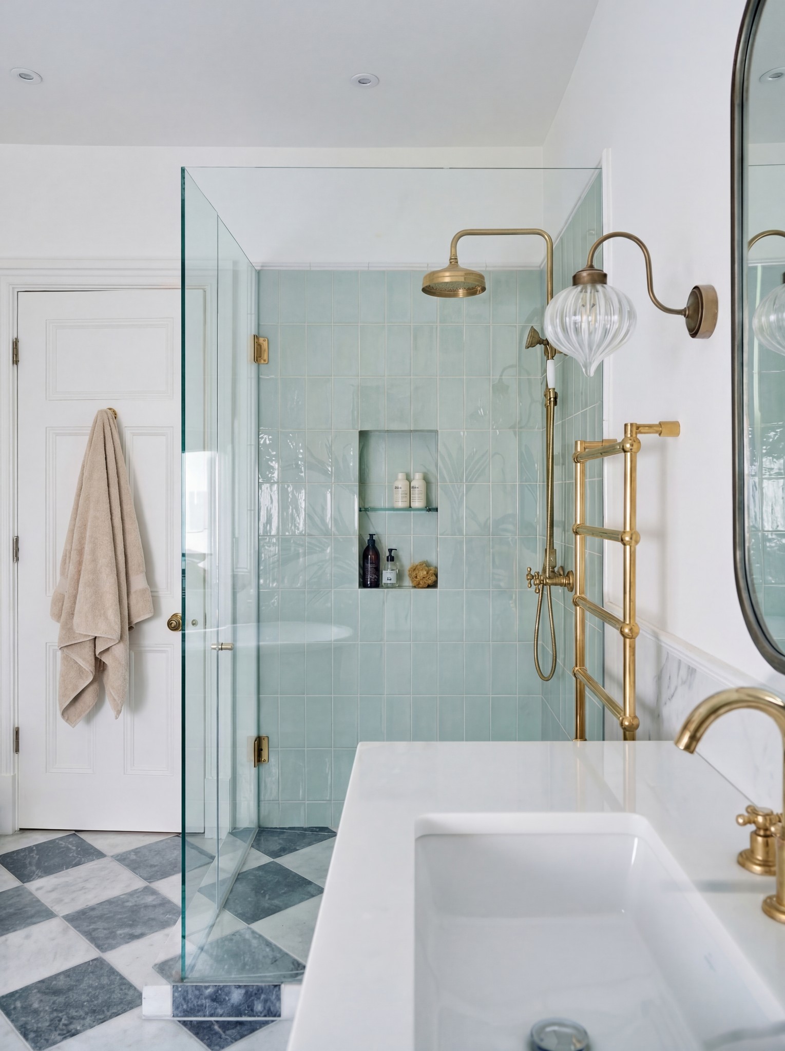 Bathroom with a glass shower enclosure, green tiles, brass fittings and patterned floor