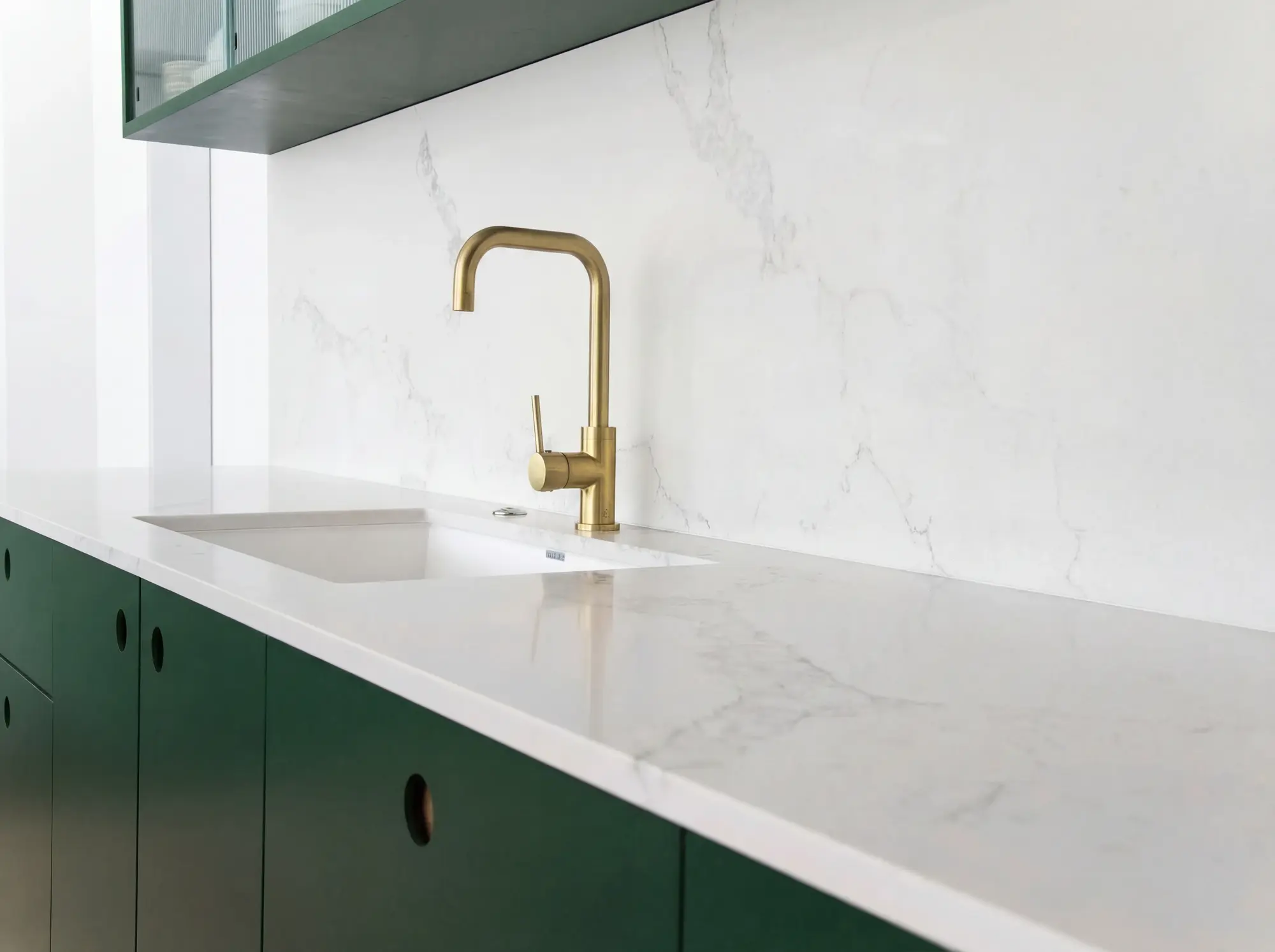 Green kitchen cabinets with a white quartz worktop and brass tap